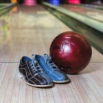 Bowling shoes and a red ball on a wooden lane, ready for action.